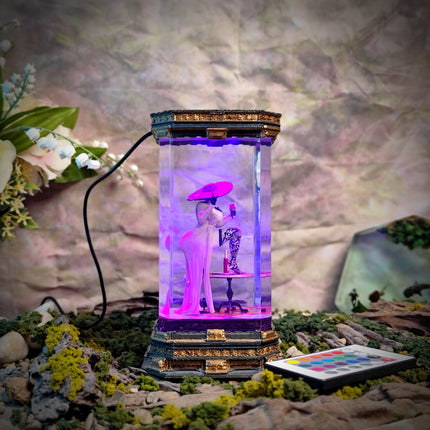 Decorative lamp with a figurine inside, surrounded by plants and flowers on a textured surface.