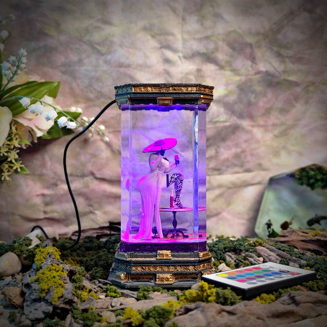 Decorative lamp with a figurine inside, surrounded by plants and flowers on a textured surface.