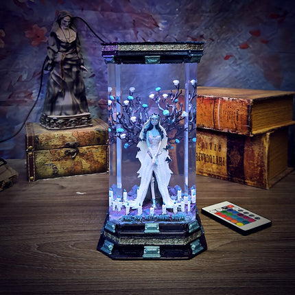 Decorative light box with a figure inside, surrounded by books and a statue on a wooden surface.