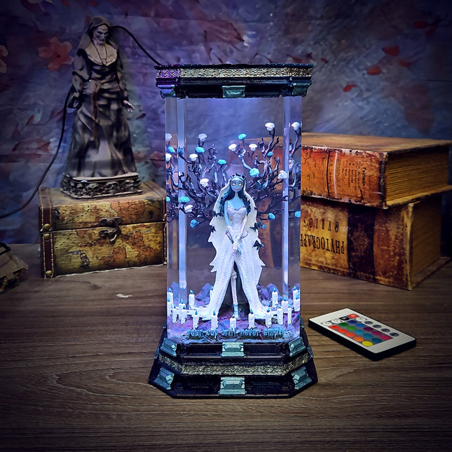 Decorative light box with a figure inside, surrounded by books and a statue on a wooden surface.