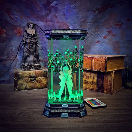 Decorative lamp with green light effects on a wooden surface, surrounded by books and a statue.