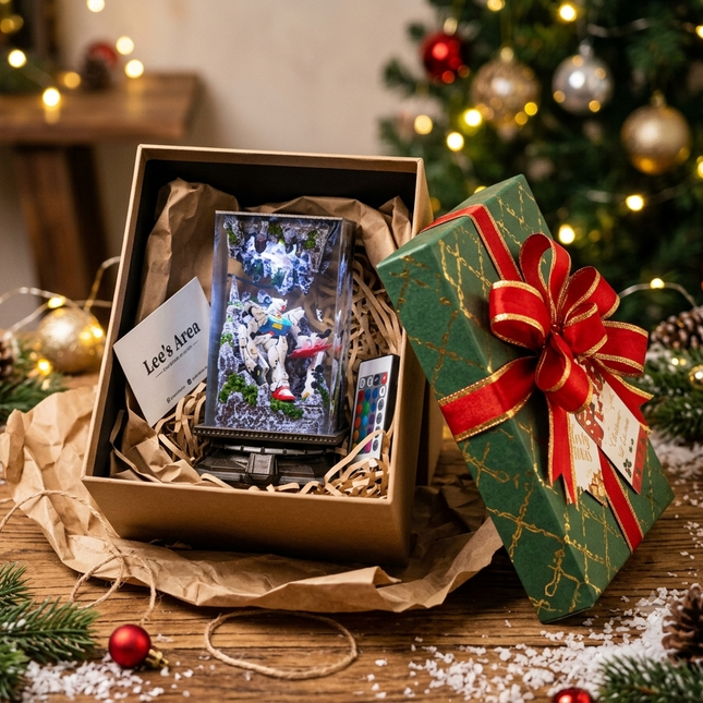 A Christmas-themed gift box set on a wooden table, featuring a brown box containing a miniature snow globe and a small card, alongside a green wrapped gift with a red bow. The background is decorated with a Christmas tree, lights, pinecones, and red ornaments.