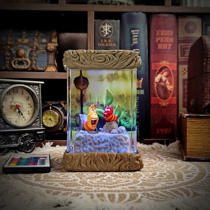 Decorative lamp with characters in a glass case on a patterned surface with books in the background