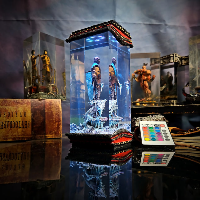 Decorative light box with figurines and a remote control on a reflective surface.